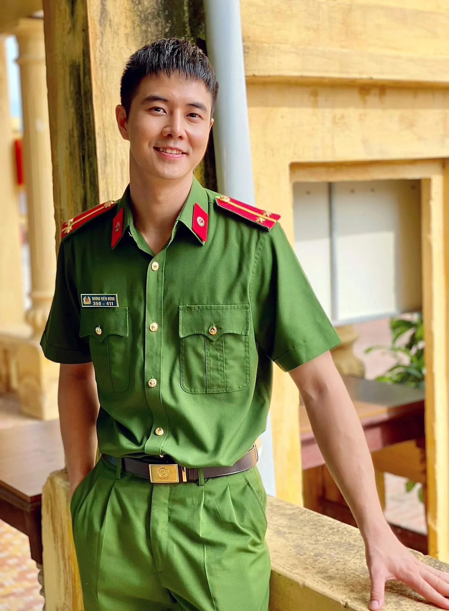 Nam công an mặc đồng phục xanh đứng trước tòa nhà