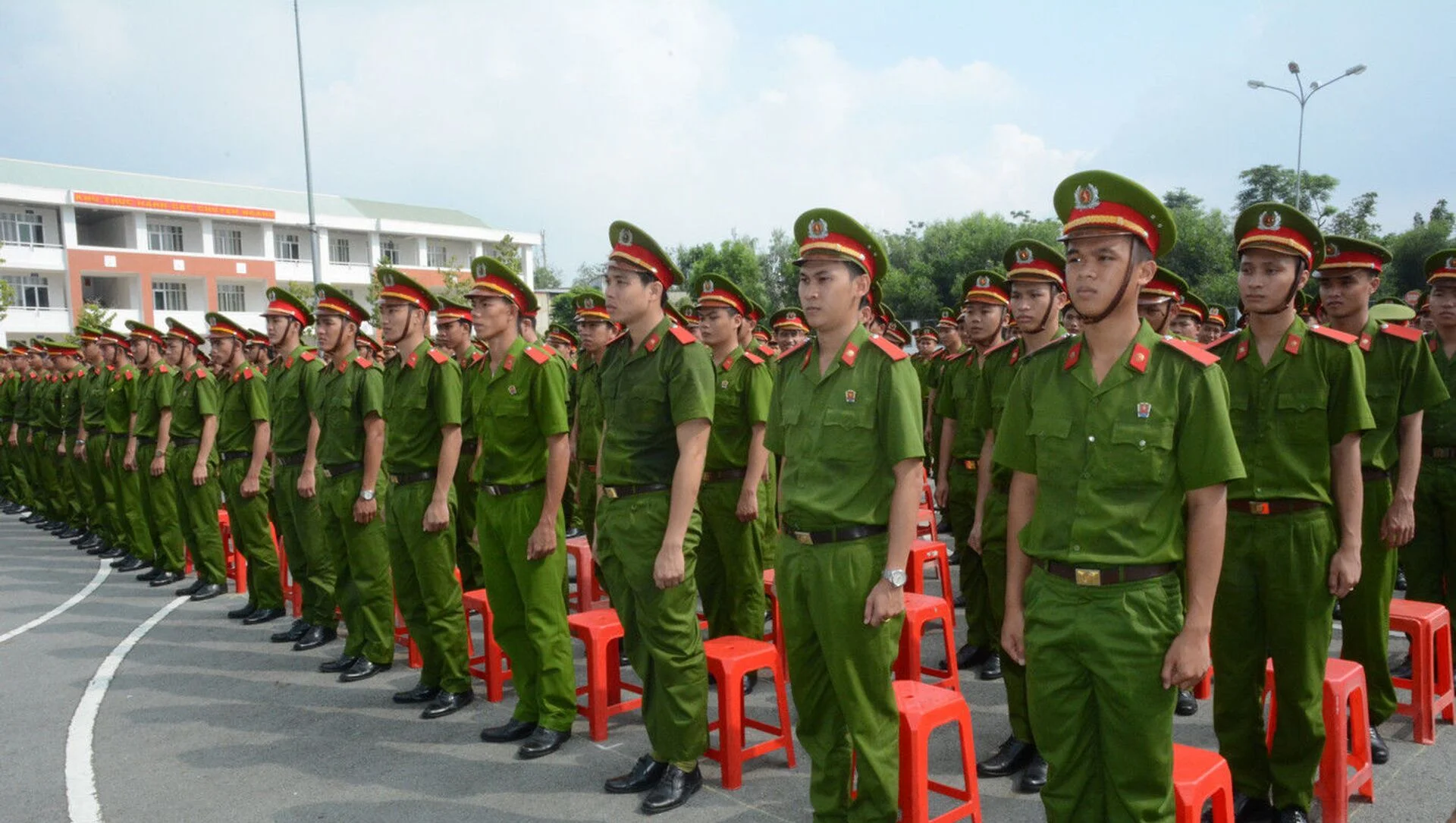 Ảnh công an Việt Nam mặc đồng phục xanh đứng thành hàng bên những chiếc ghế đỏ tại sân ngoài trời