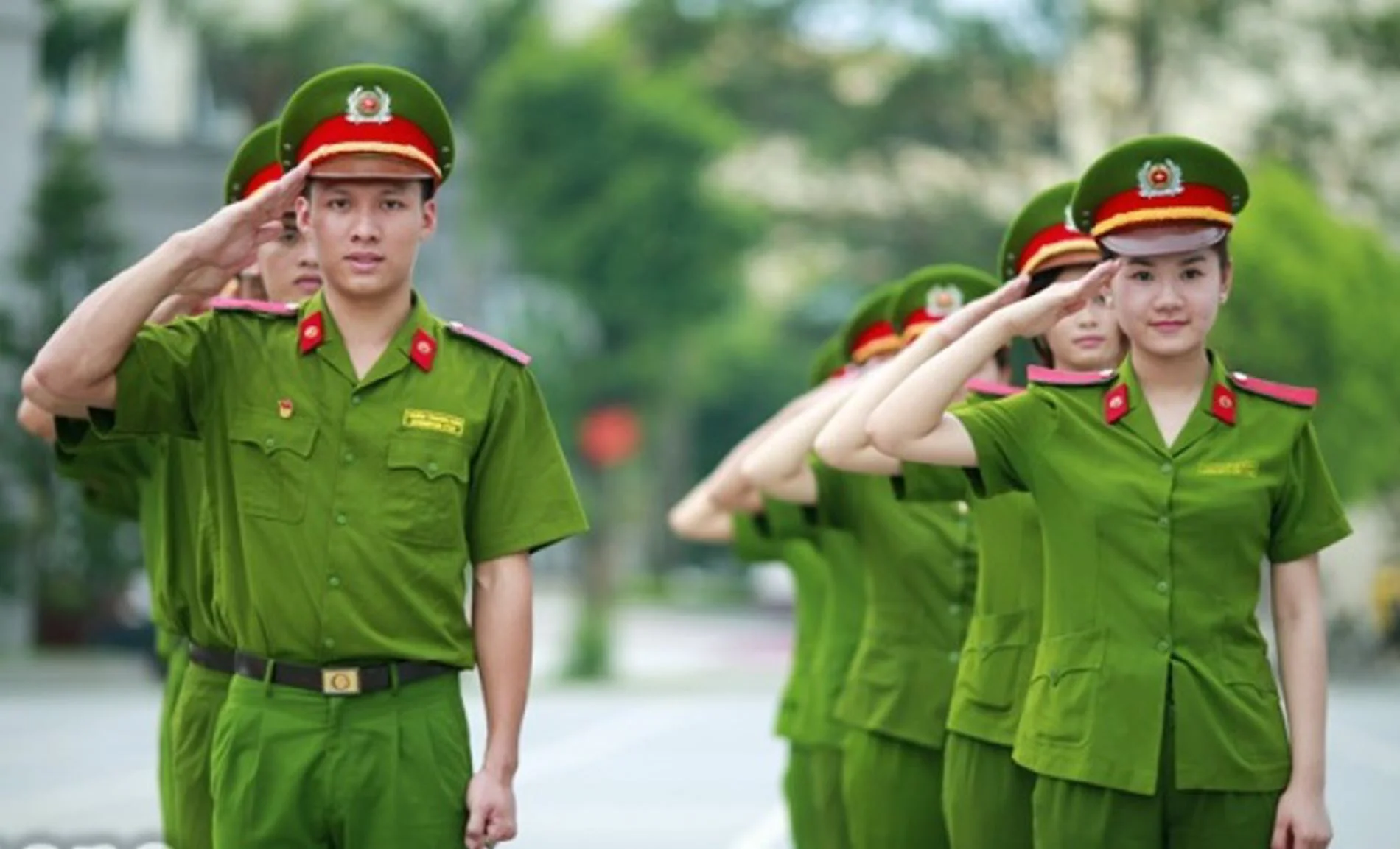 Ảnh công an nam nữ mặc đồng phục xanh đang chào theo đội hình trên đường phố