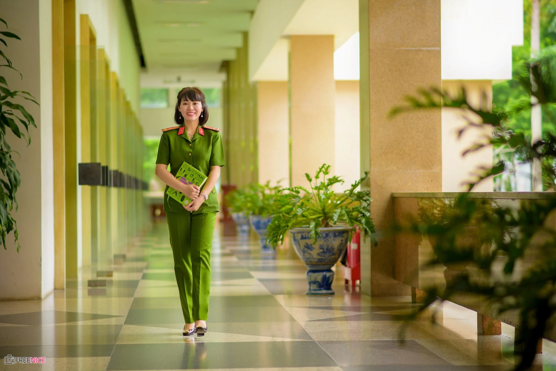 Nữ công an đứng trong hành lang sáng rộng có nhiều cây xanh