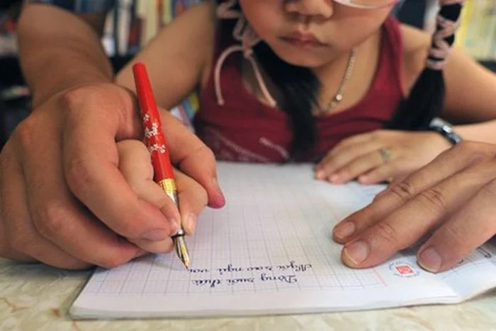 Bàn tay người lớn đang hướng dẫn trẻ em tập viết trong giờ học tập
