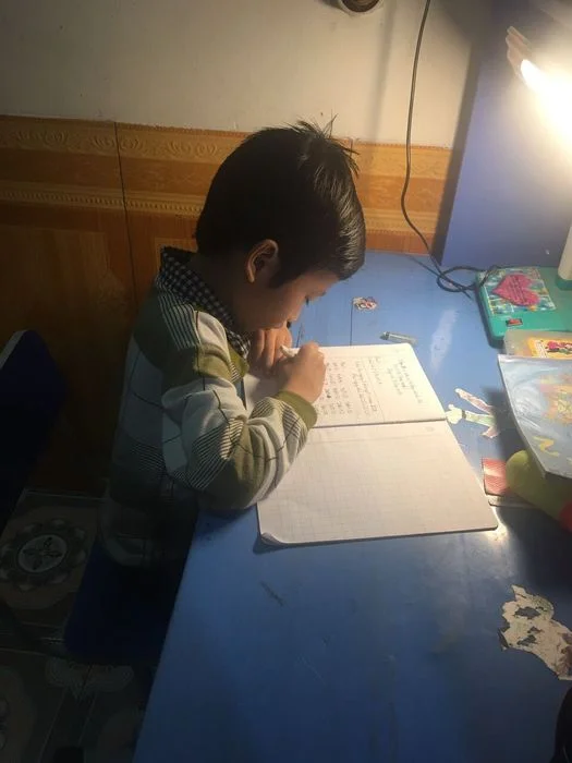 Học sinh nhỏ tuổi đang chăm chú học tập dưới ánh đèn bàn