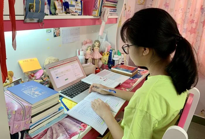 Nữ sinh đang tập trung vào việc học tập với máy tính và sách vở tại nhà.