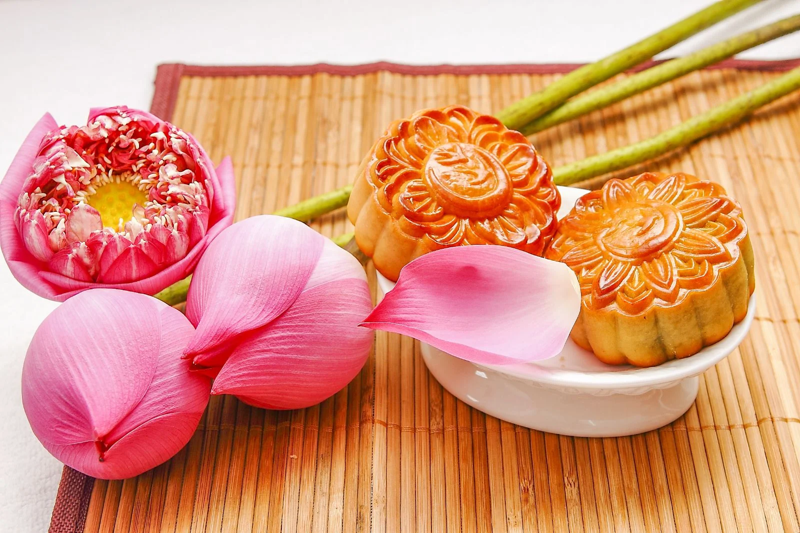 Bánh Trung Thu họa tiết hoa đặt cạnh cánh sen hồng trên khay trắng